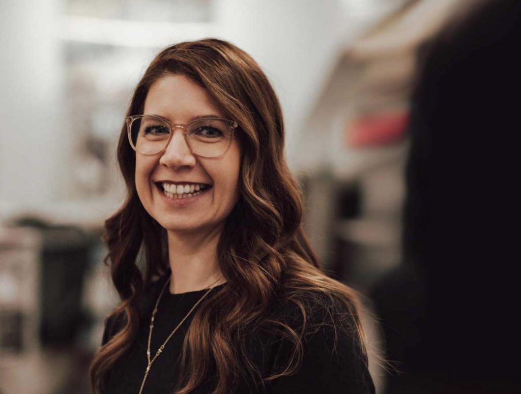 Johanna Schubert: Deine Brautstylistin aus Regensburg: Nahaufnahme einer lächelnden Frau mit langen, gewellten Haaren und Brille. Professioneller Auftritt für individuelles Hochzeitsstyling in Regensburg und Umgebung.